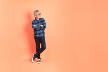 Koyu mavi ekose gömlekli yaşlı bir Asyalı şeftali pembesi bir arka plana karşı duruyor..