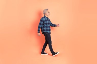 Koyu mavi ekose gömlekli yaşlı bir Asyalı şeftali pembesi bir arka plana karşı duruyor..