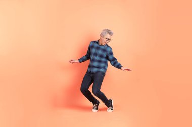 Koyu mavi ekose gömlekli yaşlı bir Asyalı şeftali pembesi bir arka plana karşı duruyor..