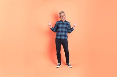 Koyu mavi ekose gömlekli yaşlı bir Asyalı şeftali pembesi bir arka plana karşı duruyor..