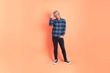 Koyu mavi ekose gömlekli yaşlı bir Asyalı şeftali pembesi bir arka plana karşı duruyor..