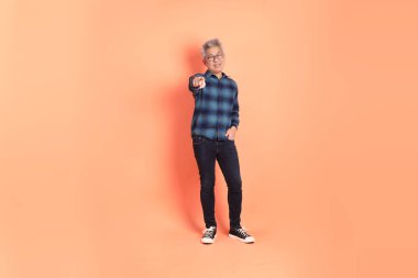 Koyu mavi ekose gömlekli yaşlı bir Asyalı şeftali pembesi bir arka plana karşı duruyor..