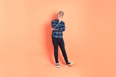 Koyu mavi ekose gömlekli yaşlı bir Asyalı şeftali pembesi bir arka plana karşı duruyor..