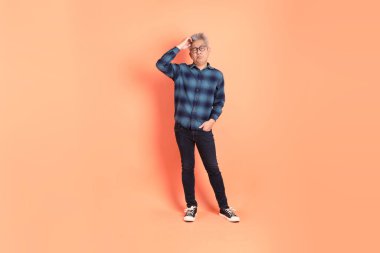 Koyu mavi ekose gömlekli yaşlı bir Asyalı şeftali pembesi bir arka plana karşı duruyor..