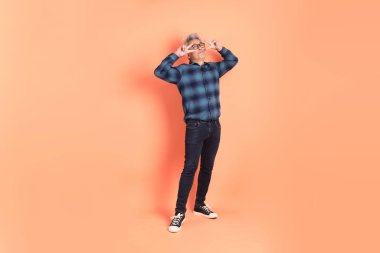 Koyu mavi ekose gömlekli yaşlı bir Asyalı şeftali pembesi bir arka plana karşı duruyor..