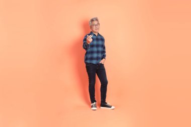 Koyu mavi ekose gömlekli yaşlı bir Asyalı şeftali pembesi bir arka plana karşı duruyor..