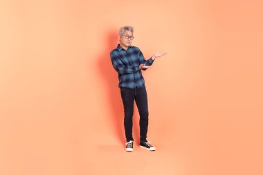 Koyu mavi ekose gömlekli yaşlı bir Asyalı şeftali pembesi bir arka plana karşı duruyor..