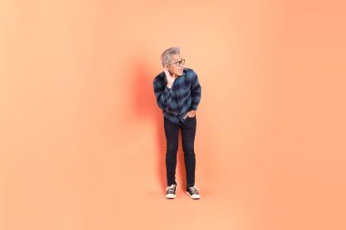 Koyu mavi ekose gömlekli yaşlı bir Asyalı şeftali pembesi bir arka plana karşı duruyor..