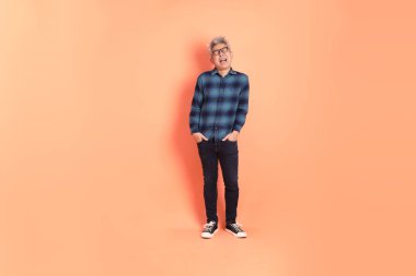 Koyu mavi ekose gömlekli yaşlı bir Asyalı şeftali pembesi bir arka plana karşı duruyor..