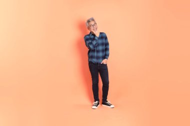 Koyu mavi ekose gömlekli yaşlı bir Asyalı şeftali pembesi bir arka plana karşı duruyor..