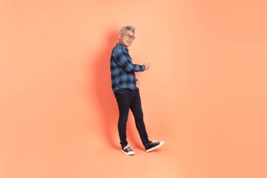 Koyu mavi ekose gömlekli yaşlı bir Asyalı şeftali pembesi bir arka plana karşı duruyor..