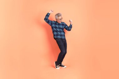 A senior East Asian man in a deep blue plaid shirt stands against a peach-pink background. clipart