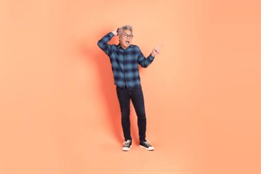 Koyu mavi ekose gömlekli yaşlı bir Asyalı şeftali pembesi bir arka plana karşı duruyor..