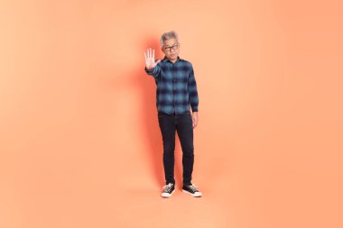 Koyu mavi ekose gömlekli yaşlı bir Asyalı şeftali pembesi bir arka plana karşı duruyor..