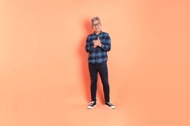 Koyu mavi ekose gömlekli yaşlı bir Asyalı şeftali pembesi bir arka plana karşı duruyor..