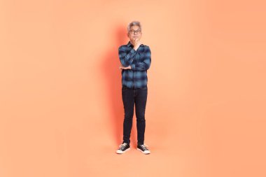 Koyu mavi ekose gömlekli yaşlı bir Asyalı şeftali pembesi bir arka plana karşı duruyor..