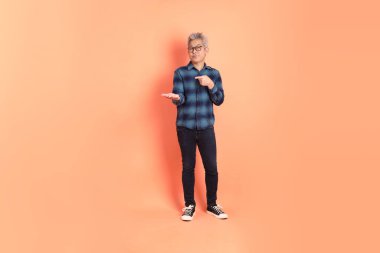 Koyu mavi ekose gömlekli yaşlı bir Asyalı şeftali pembesi bir arka plana karşı duruyor..