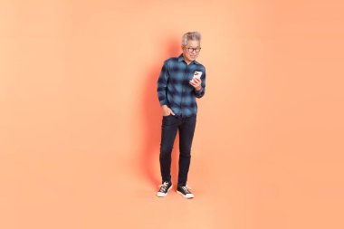 Koyu mavi ekose gömlekli yaşlı bir Asyalı şeftali pembesi bir arka plana karşı duruyor..