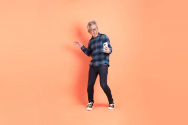 Koyu mavi ekose gömlekli yaşlı bir Asyalı şeftali pembesi bir arka plana karşı duruyor..