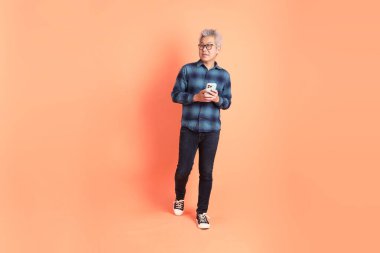 Koyu mavi ekose gömlekli yaşlı bir Asyalı şeftali pembesi bir arka plana karşı duruyor..