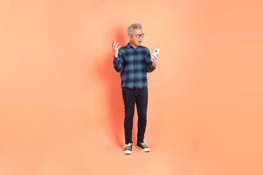 Koyu mavi ekose gömlekli yaşlı bir Asyalı şeftali pembesi bir arka plana karşı duruyor..