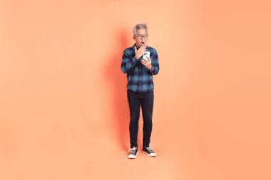 Koyu mavi ekose gömlekli yaşlı bir Asyalı şeftali pembesi bir arka plana karşı duruyor..