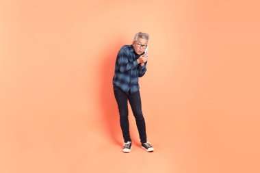 Koyu mavi ekose gömlekli yaşlı bir Asyalı şeftali pembesi bir arka plana karşı duruyor..