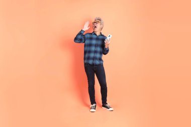 Koyu mavi ekose gömlekli yaşlı bir Asyalı şeftali pembesi bir arka plana karşı duruyor..