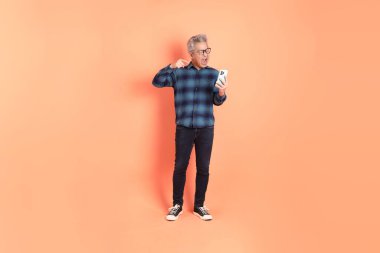 Koyu mavi ekose gömlekli yaşlı bir Asyalı şeftali pembesi bir arka plana karşı duruyor..