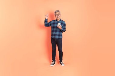 Koyu mavi ekose gömlekli yaşlı bir Asyalı şeftali pembesi bir arka plana karşı duruyor..