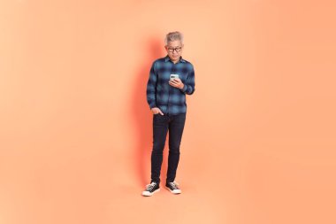 Koyu mavi ekose gömlekli yaşlı bir Asyalı şeftali pembesi bir arka plana karşı duruyor..