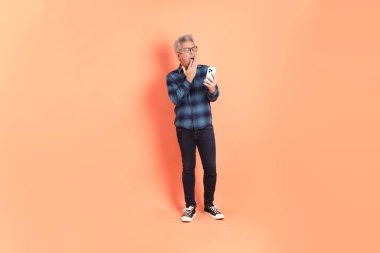 Koyu mavi ekose gömlekli yaşlı bir Asyalı şeftali pembesi bir arka plana karşı duruyor..