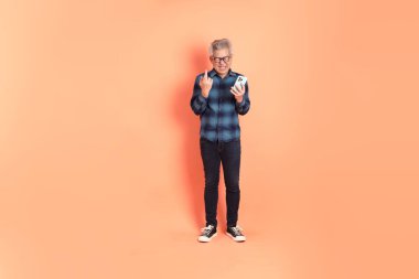 Koyu mavi ekose gömlekli yaşlı bir Asyalı şeftali pembesi bir arka plana karşı duruyor..