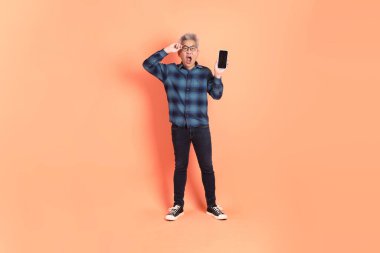 Koyu mavi ekose gömlekli yaşlı bir Asyalı şeftali pembesi bir arka plana karşı duruyor..