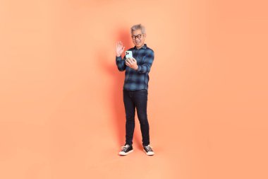 Koyu mavi ekose gömlekli yaşlı bir Asyalı şeftali pembesi bir arka plana karşı duruyor..