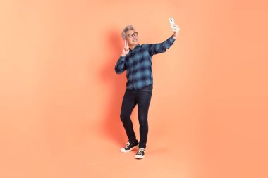 Koyu mavi ekose gömlekli yaşlı bir Asyalı şeftali pembesi bir arka plana karşı duruyor..