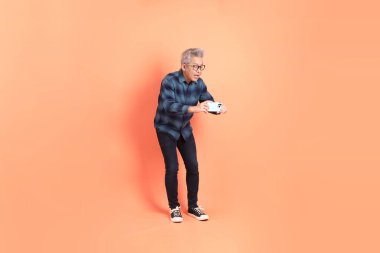 Koyu mavi ekose gömlekli yaşlı bir Asyalı şeftali pembesi bir arka plana karşı duruyor..