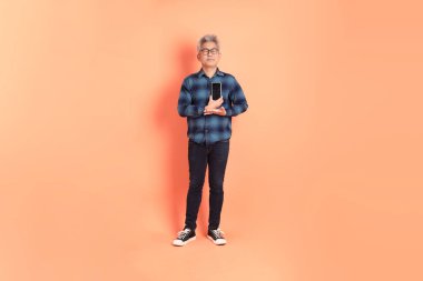 Koyu mavi ekose gömlekli yaşlı bir Asyalı şeftali pembesi bir arka plana karşı duruyor..