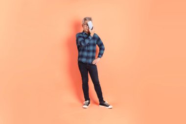 Koyu mavi ekose gömlekli yaşlı bir Asyalı şeftali pembesi bir arka plana karşı duruyor..