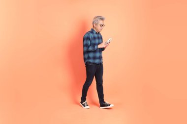 Koyu mavi ekose gömlekli yaşlı bir Asyalı şeftali pembesi bir arka plana karşı duruyor..