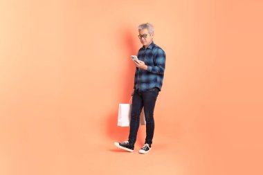 Koyu mavi ekose gömlekli yaşlı bir Asyalı şeftali pembesi bir arka plana karşı duruyor..