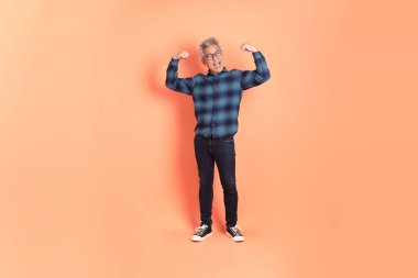 Koyu mavi ekose gömlekli yaşlı bir Asyalı şeftali pembesi bir arka plana karşı duruyor..