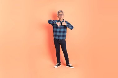 Koyu mavi ekose gömlekli yaşlı bir Asyalı şeftali pembesi bir arka plana karşı duruyor..