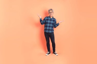 Koyu mavi ekose gömlekli yaşlı bir Asyalı şeftali pembesi bir arka plana karşı duruyor..