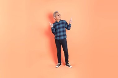 Koyu mavi ekose gömlekli yaşlı bir Asyalı şeftali pembesi bir arka plana karşı duruyor..