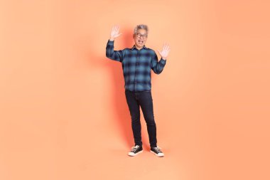 Koyu mavi ekose gömlekli yaşlı bir Asyalı şeftali pembesi bir arka plana karşı duruyor..