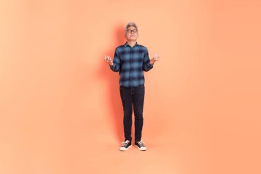 Koyu mavi ekose gömlekli yaşlı bir Asyalı şeftali pembesi bir arka plana karşı duruyor..