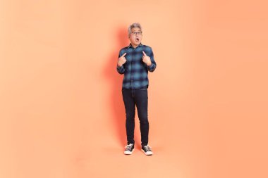 Koyu mavi ekose gömlekli yaşlı bir Asyalı şeftali pembesi bir arka plana karşı duruyor..