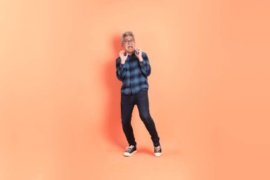 Koyu mavi ekose gömlekli yaşlı bir Asyalı şeftali pembesi bir arka plana karşı duruyor..