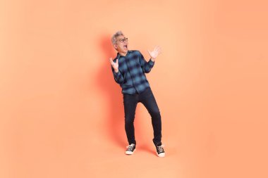 Koyu mavi ekose gömlekli yaşlı bir Asyalı şeftali pembesi bir arka plana karşı duruyor..